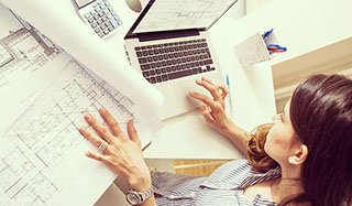 White woman architect sitting at desk with plans and laptop