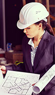 White woman architect standing looking at plans wearing construction hat
