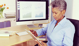 Older african woman sitting at desk working on a tablet